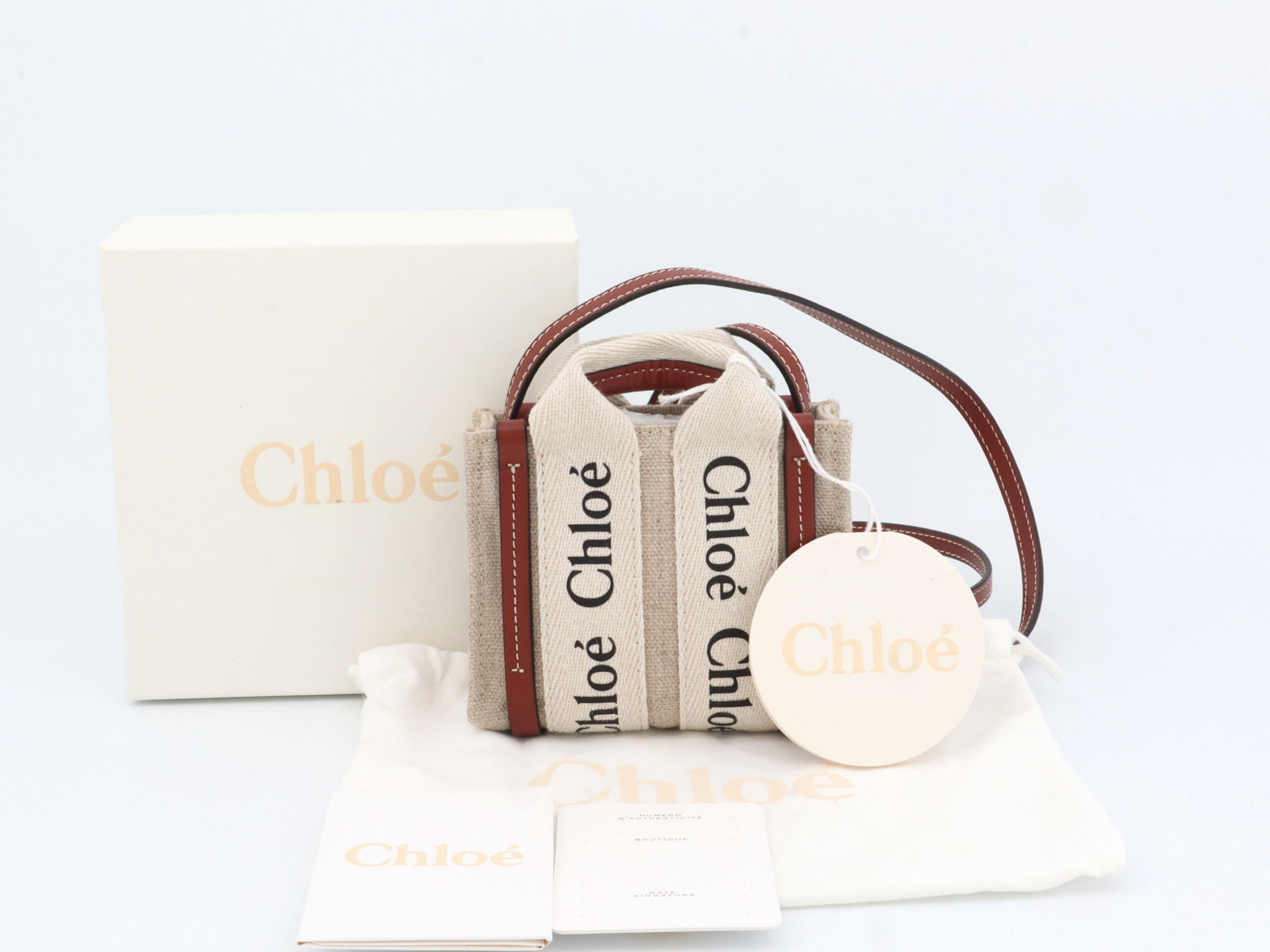 Chloé Woody Nano Canvas and Leather 2-Way Bag with Box & Tags, Giftable Condition: Authentic Chloe Mini structured bag in beige canvas with repeated Chloé logo webbing on front and back panels. Brown leather trim along edges and base. Top handles and long leather shoulder str