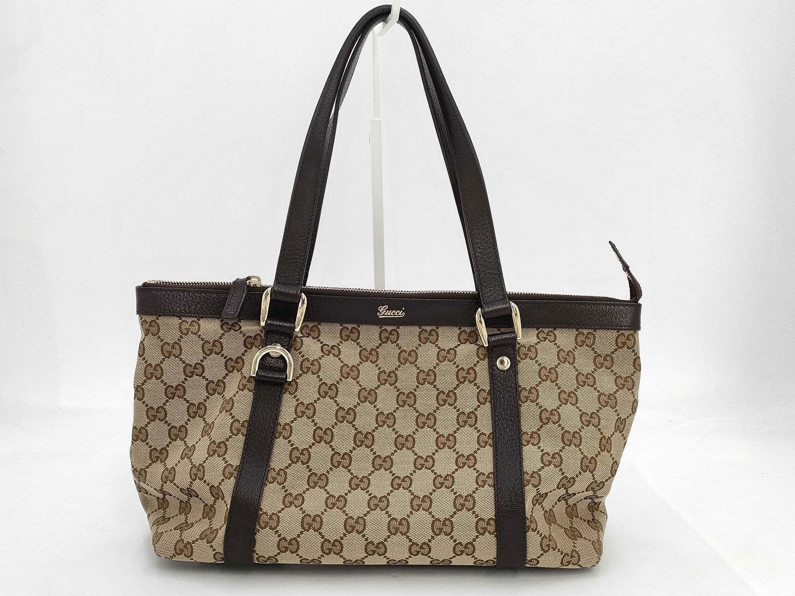 Gucci GG Canvas & Leather Tote Bag: Tote bag featuring beige canvas printed with the brown GG pattern and trimmed with dark brown leather along the top edge, straps, and base. Having two leather shoulder straps with buckle accents and g