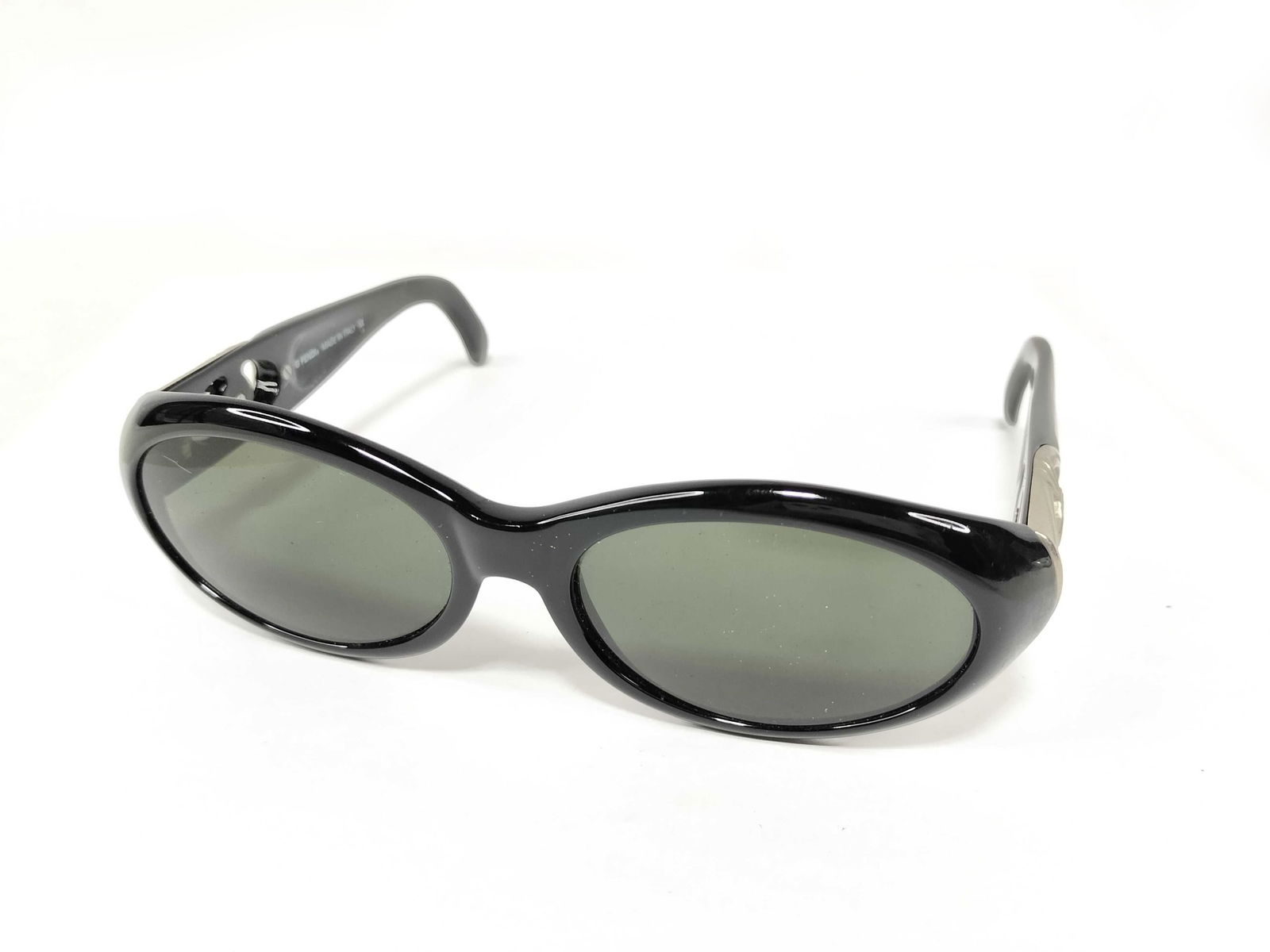 Fendi Oval Sunglasses with major Aura: Authentic Fendi Oval Sunglasses. Sunglasses having a glossy black frame with oval green-tinted lenses. Featuring wide arms accented with silver-tone Fendi logo plaques. Interior arms marked with model