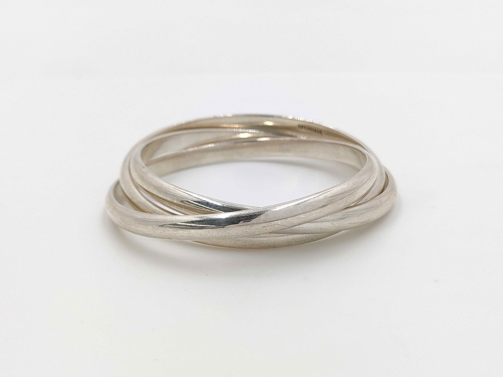 Tiffany & Co. Trinity Sterling Silver Bracelet: Authentic Tiffany & Co. Trinity Sterling Silver Bracelet. Bracelet featuring three interlocking sterling silver bangles in a rolling design. Each band is smooth and rounded, and the interior is ma