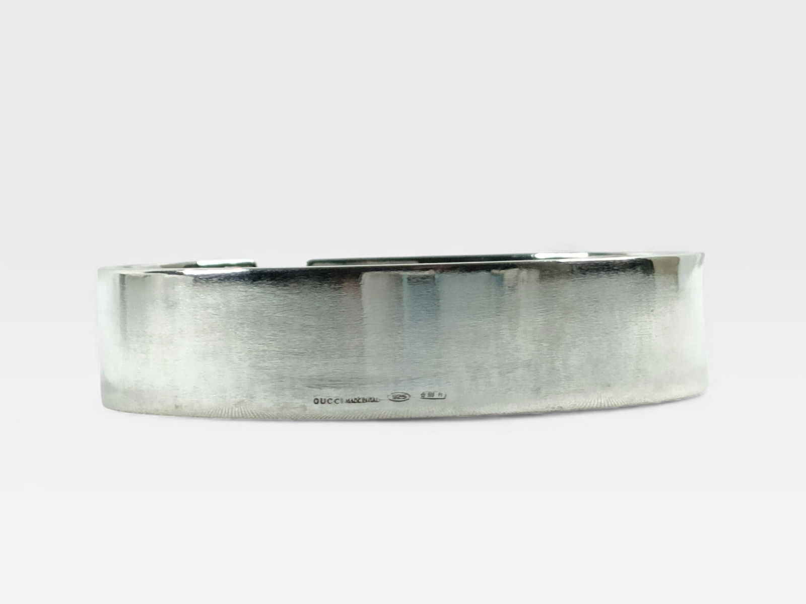 Gucci Sterling Silver Cutout Bangle: Authentic Gucci Wide sterling silver bangle with brushed exterior finish. Smooth interior with polished surface. Slightly oval shape with open cuff-style gap for fit. Gucci and metal hallmarks engrave