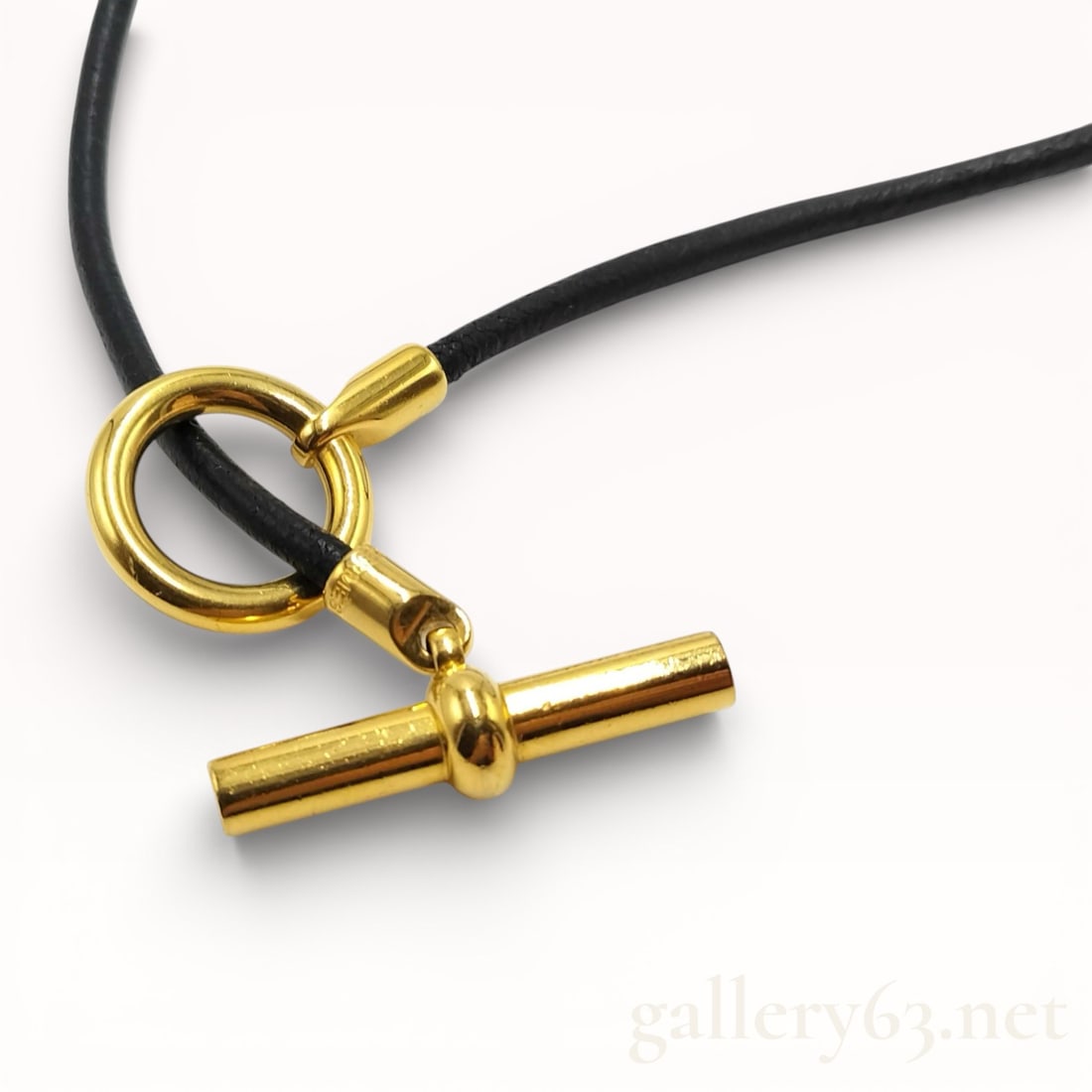 Hermès Glenan Leather Choker Necklace With Gold-Tone Hardware: Hermès Glenan choker necklace featuring a black leather cord and gold-tone hardware. Designed with a circular ring and horizontal toggle-style bar closure. Smooth leather construction with poli