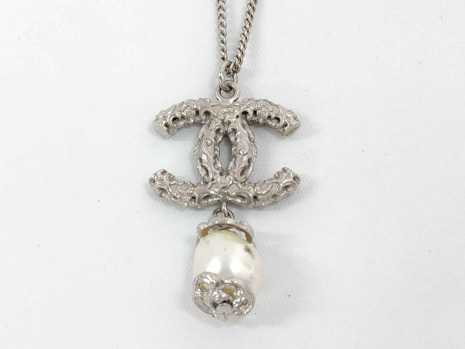 Chanel B14A CC Logo Pearl Drop Pendant Necklace 24"/60cm: Chanel necklace having a silver-tone metal cable chain set with a rhinestone-set interlocking CC pendant. Pendant suspending a single white faux pearl drop capped with silver-tone detailing. Lobster c