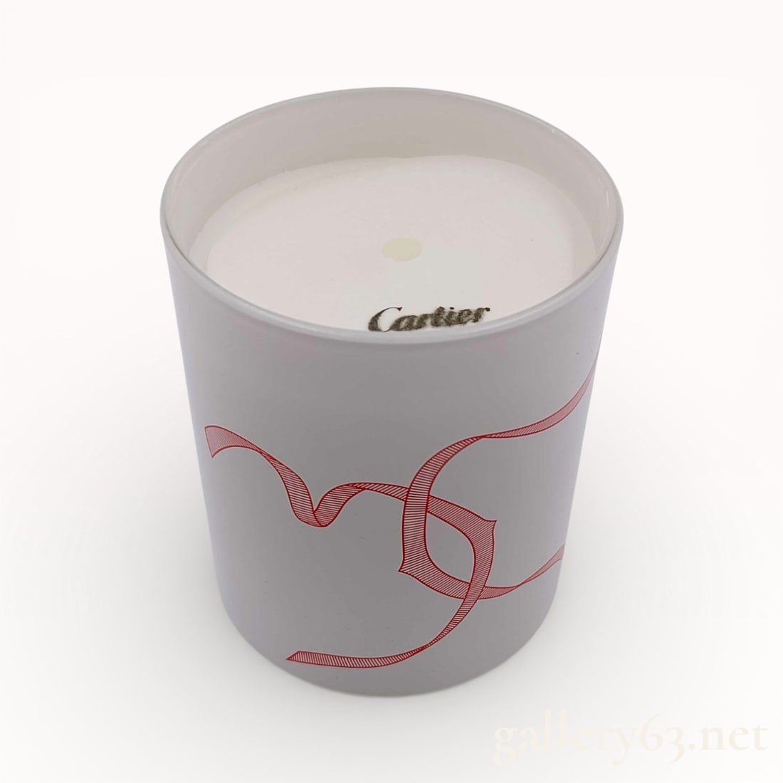 Cartier Signature Scented Candle: Authentic Cartier Scented candle presented in a cylindrical gray vessel featuring a red graphic motif wrapping the exterior. White wax interior with a single centered wick. Cartier logo
