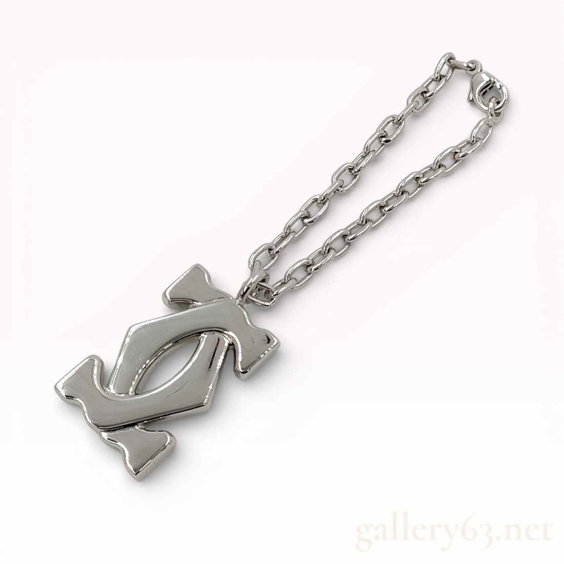 Cartier 2C Logo Charm with box & pouch: Polished silver-tone charm featuring the interlocking double C motif forming the Cartier 2C design. Sculptural openwork form with rounded contours and smooth reflective surfaces. Attached silver-tone