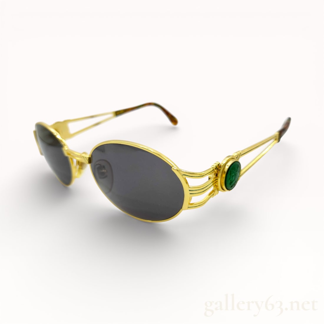 Fendi Tortoiseshell SL7035 Oval Sunglasses: Fendi sunglasses having oval dark-tinted lenses set within gold-tone metal frames. Decorative openwork temples featuring green cabochon-style medallion accents near the hinges. Slim metal arms termina