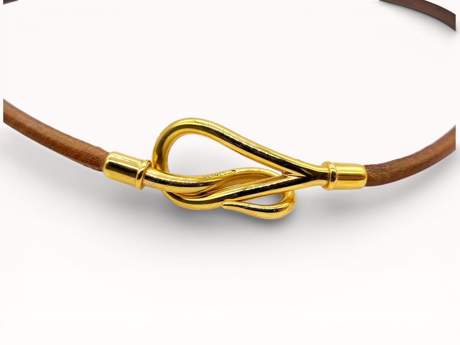Hermès Leather Choker Necklace with Gilt Hook Clasp: Authentic Hermès choker necklace constructed of smooth brown leather cord, finished with a sculptural gilt metal hook-and-loop clasp. Design presenting a continuous circular profile, the clasp