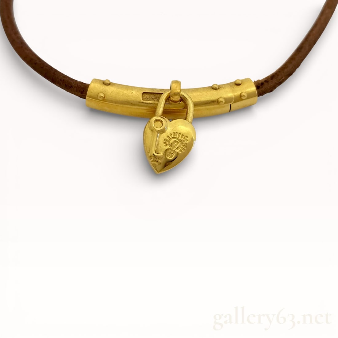 Hermès Heart Cadena Viviride Leather Necklace: Authentic Hermès necklace featuring a brown leather cord set with a gold-tone metal bar clasp. Heart-shaped Cadena padlock charm suspended at center, having embossed Hermès branding and decorative m