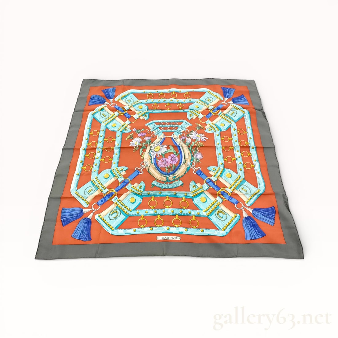 Hermès Field Silk Carré Scarf: Hermès silk carré scarf featuring the Field design, rendered in rust, gray, turquoise, blue, and gold tones. Symmetrical composition presents equestrian tack, straps, and tassels arranged in a geome