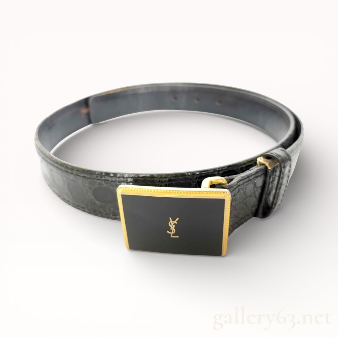 Yves Saint Laurent Logo Buckle Leather Belt: Authentic Yves Saint Laurent belt featuring a black leather strap having a subtle textured finish. Rectangular buckle set with a black enamel face framed by a gold-tone border. Center displaying an ap