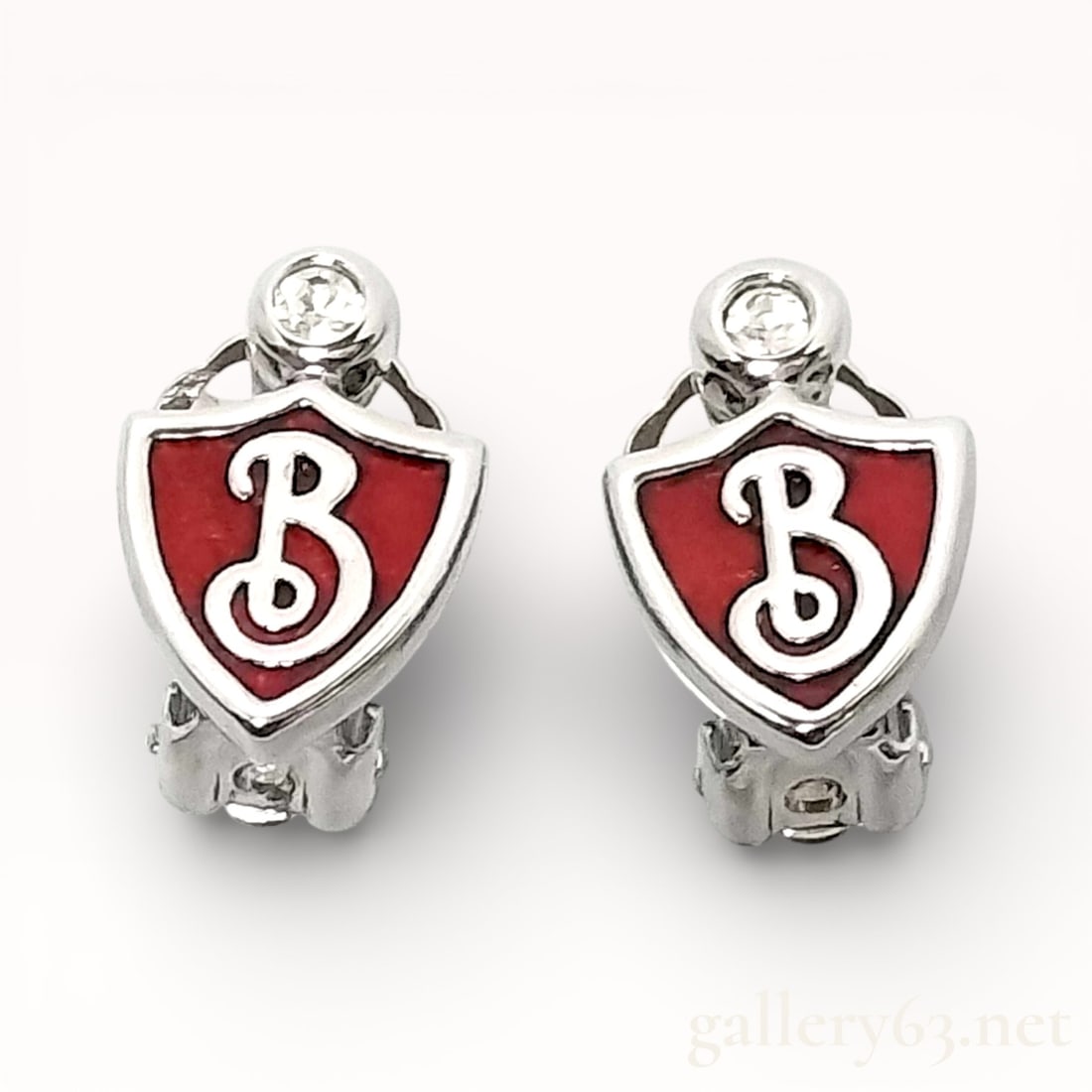 Burberry Shield Logo Clip-On Earrings: Authentic Burberry earrings featuring a silver-tone metal construction in a shield-shaped form. Red enamel shield centers set with raised Burberry “B” logo detailing. Clear round accent