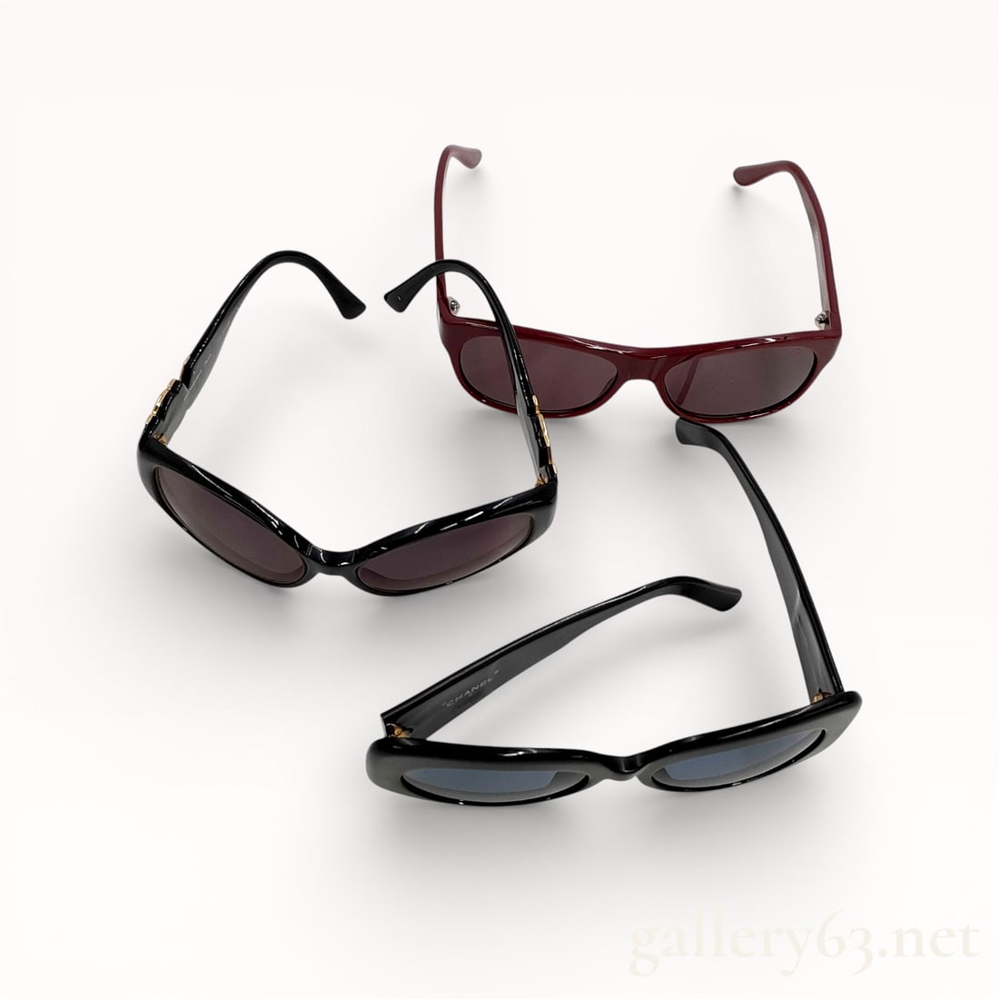 Designer Sunglasses Assortment Including Chanel, Gucci, and Yves Saint Laurent: Group of three pairs of designer sunglasses featuring varied frame styles and colorways. Assortment including black, burgundy, and dark-toned frames with tinted lenses. Mixed silhouettes ranging from