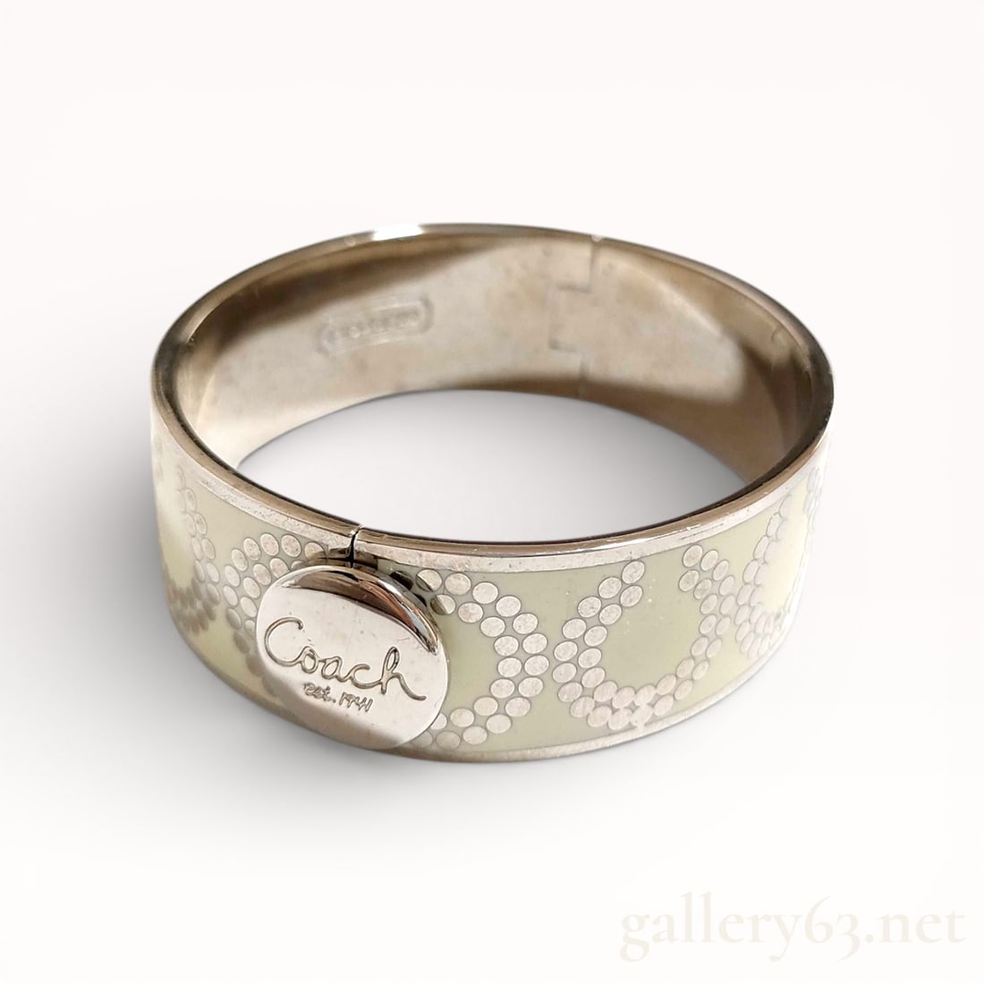 Coach Logo Hinged Bangle Bracelet: Authentic Coach bangle bracelet formed in a hinged metal construction with a polished silver-tone finish. Exterior decorated with a repeating Coach signature motif rendered in a dotted pattern. Front