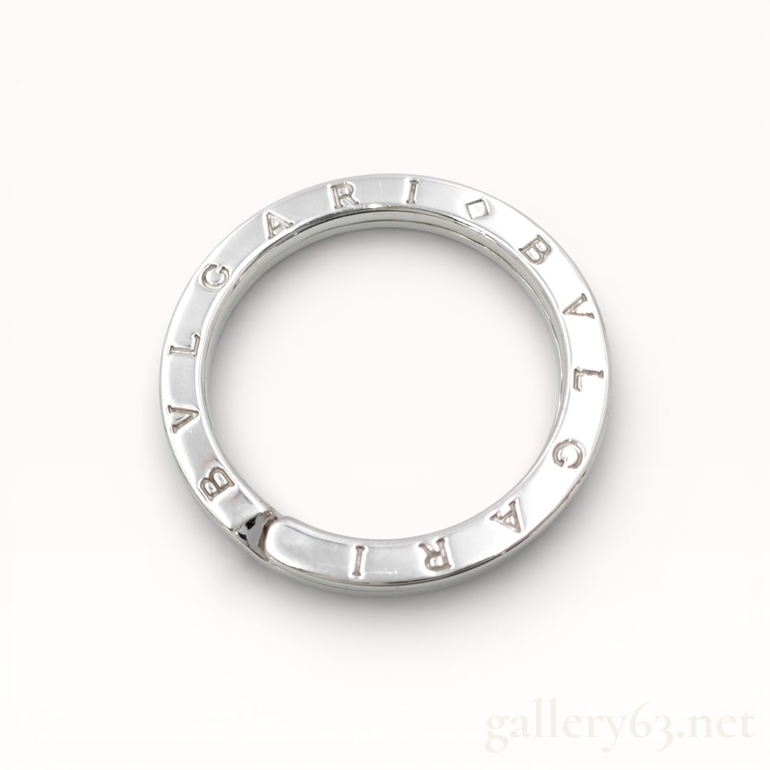 Bvlgari Logo Ring Keychain Charm: Authentic Bvlgari keychain charm formed as a circular ring with a polished silver-tone finish. Outer edge engraved with the Bvlgari name repeated around the circumference. Ring featuring a hinged open