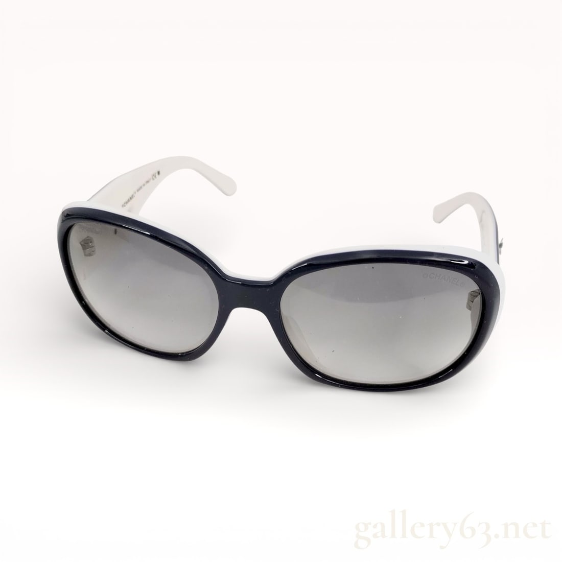 Chanel Camellia Model 5113 Sunglasses in Blue/White: Authentic Chanel Camellia model 5113 sunglasses featuring a navy blue oval frame fitted with grey-tinted lenses. Arms finished in contrasting white, accented with Camellia motif detailing at the templ