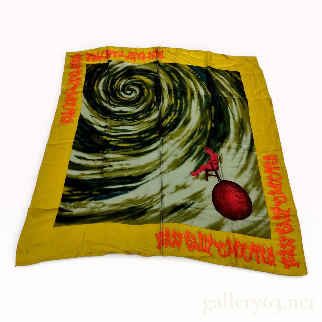 Jean Paul Gaultier Large-Format Silk Scarf: Authentic Jean Paul Gaultier silk scarf presented in a large square format. Graphic central composition depicting a swirling vortex motif with a suspended red orb element. Design framed by a contrasti