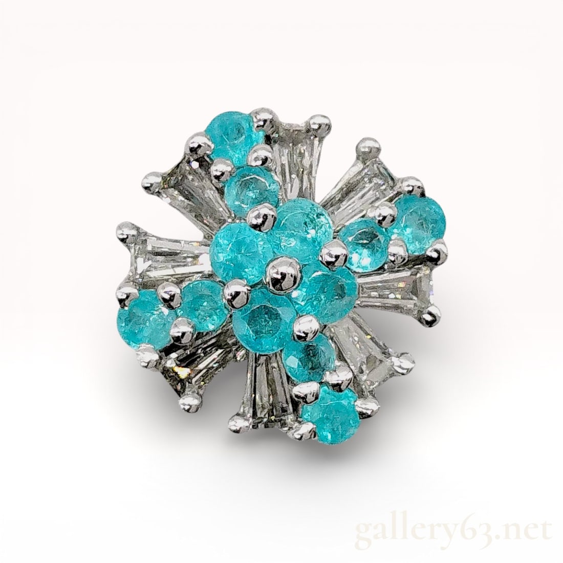 18k White Gold Paraiba Tourmaline and Diamond Cluster Pendant: 18k white gold pendant top having multiple round Paraiba tourmalines arranged in a clustered floral formation. Design accented by radiating tapered baguette-cut diamonds positioned between the tourmal