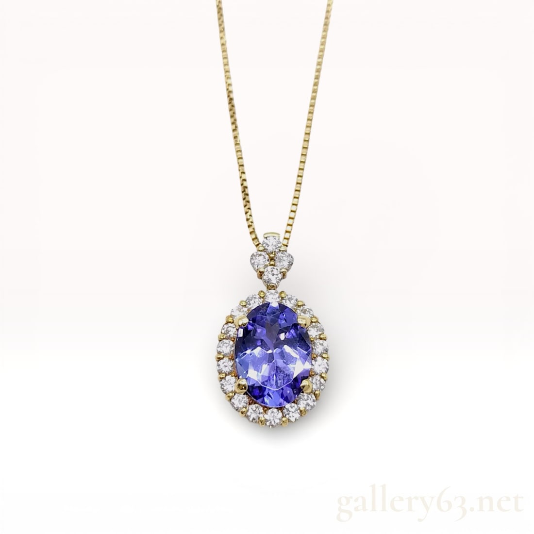 18k Yellow Gold Tanzanite and Diamond Halo Pendant Necklace: 18k yellow gold necklace having an oval-cut .97ct tanzanite center stone, framed by a .25ct halo of round brilliant-cut diamonds. Pendant featuring a scalloped gallery with openwork sides, allowing li