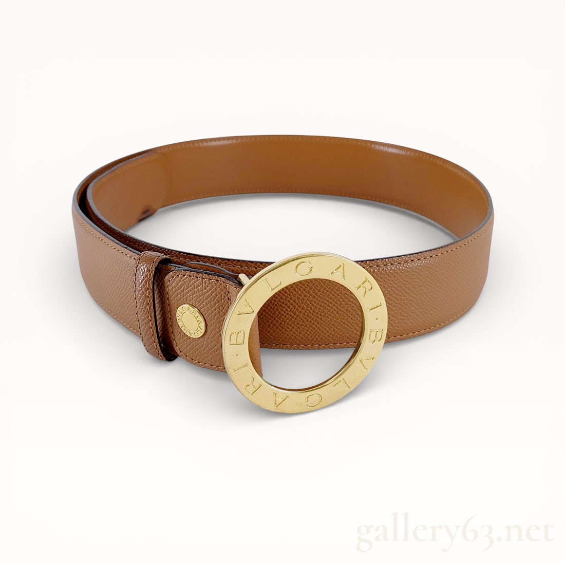 Bvlgari Camel Leather Belt: Authentic Bvlgari camel-colored leather belt, having a smooth grained exterior and finished edges. Design featuring a circular gold-tone buckle engraved with lettering around the perimeter. Constructi