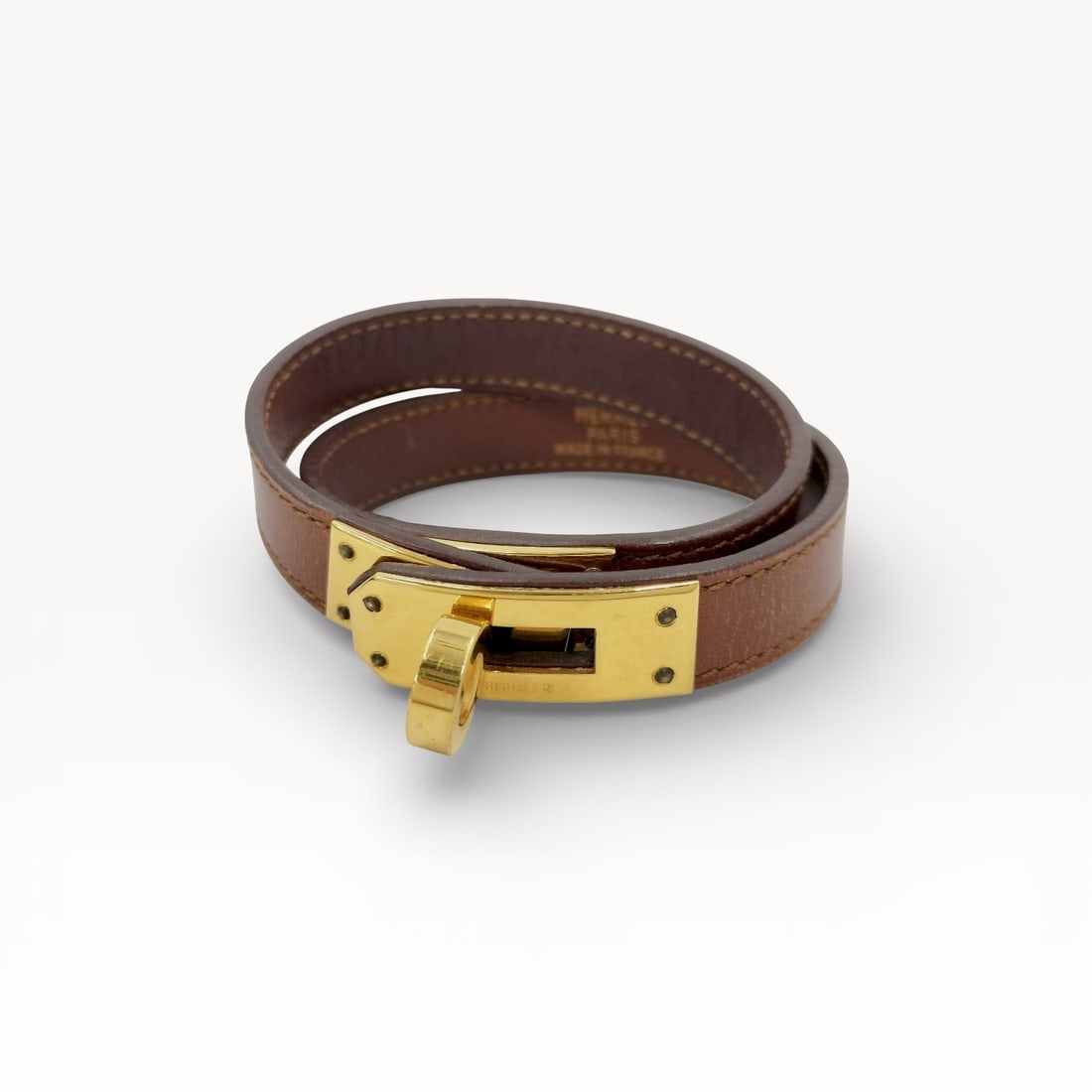 Hermès Kelly Double Tour Leather Bracelet with Gold-Tone Hardware in Brown: Authentic Hermès Kelly double tour bracelet in brown leather with gold-tone hardware. The design features the iconic Kelly turn-lock closure with stitched leather strap that wraps twice around the wr