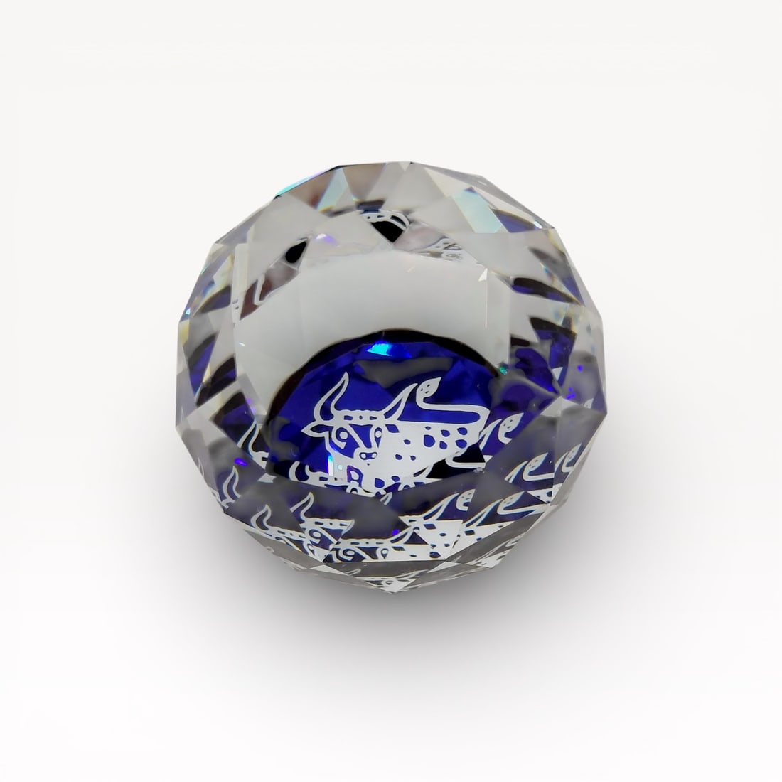 Swarovski Faceted Crystal Paperweight Year of the Ox: Authentic Swarovski paperweight in clear faceted crystal. Rounded, multi-faceted form centered with a blue medallion motif, visible through the crystal body. Flat base fitted with protective pad. Mark