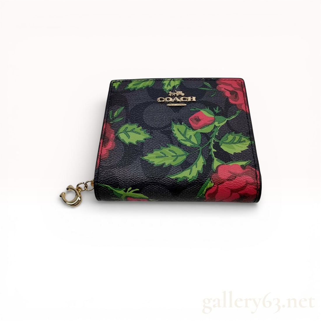 Coach Signature Floral Compact Wallet with Gold-Tone Hardware: Coach compact wallet featuring a signature coated canvas exterior with floral print overlay. Folded construction in black with red and green botanical motifs. Front displaying Coach logo stamp. Snap c