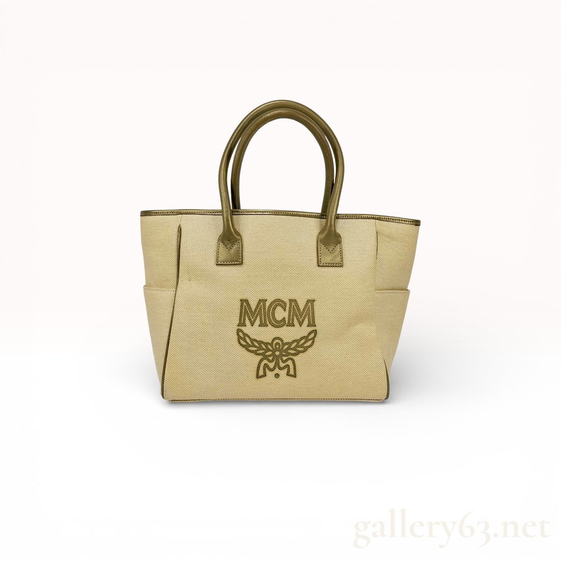 MCM Himmel Medium Sand Beige Canvas Shopper Tote Bag: Authentic MCM Himmel medium canvas tote bag featuring a structured silhouette in sand beige textile. Front exterior featuring the MCM logo print with laurel motif at center. Dual leather top handles w