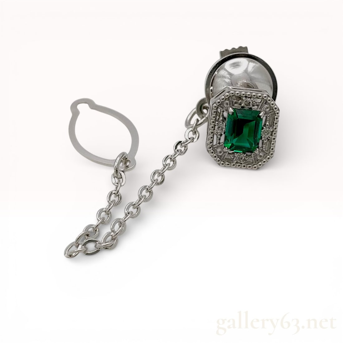 18K White Gold Emerald and Diamond Tie Pin with Chain Accent: 18K white gold tie pin featuring an emerald in an emerald-cut form, framed by a halo of small diamond accents. Design presents a geometric rectangular profile with fine milgrain-style detailing around