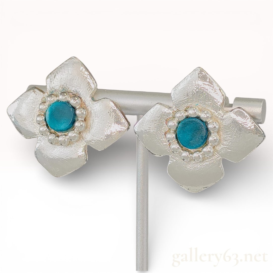 Yves Saint Laurent Silver-Tone Flower Clip Earrings with Blue Centers: Yves Saint Laurent earrings having four-petal flower forms with broad textured petals arranged around raised central setting. Centers featuring round blue cabochon-style stones held in circular bezel