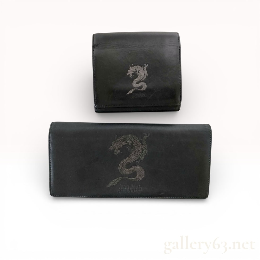 Jean Paul Gaultier Black Leather Dragon Wallet Set (2 Pieces): Set includes one long wallet and one bi-fold wallet in black leather. Both pieces feature embroidered dragon motif on front. Long wallet with multiple card slots, bill compartments, and interior zip p