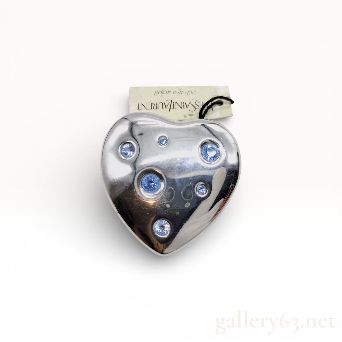 Yves Saint Laurent Heart Brooch in Silver-Tone Metal with Blue Crystal Accents: Yves Saint Laurent heart brooch featuring a polished silver-tone metal body. Puffy heart form having a smooth high-shine surface. Front set with multiple round blu