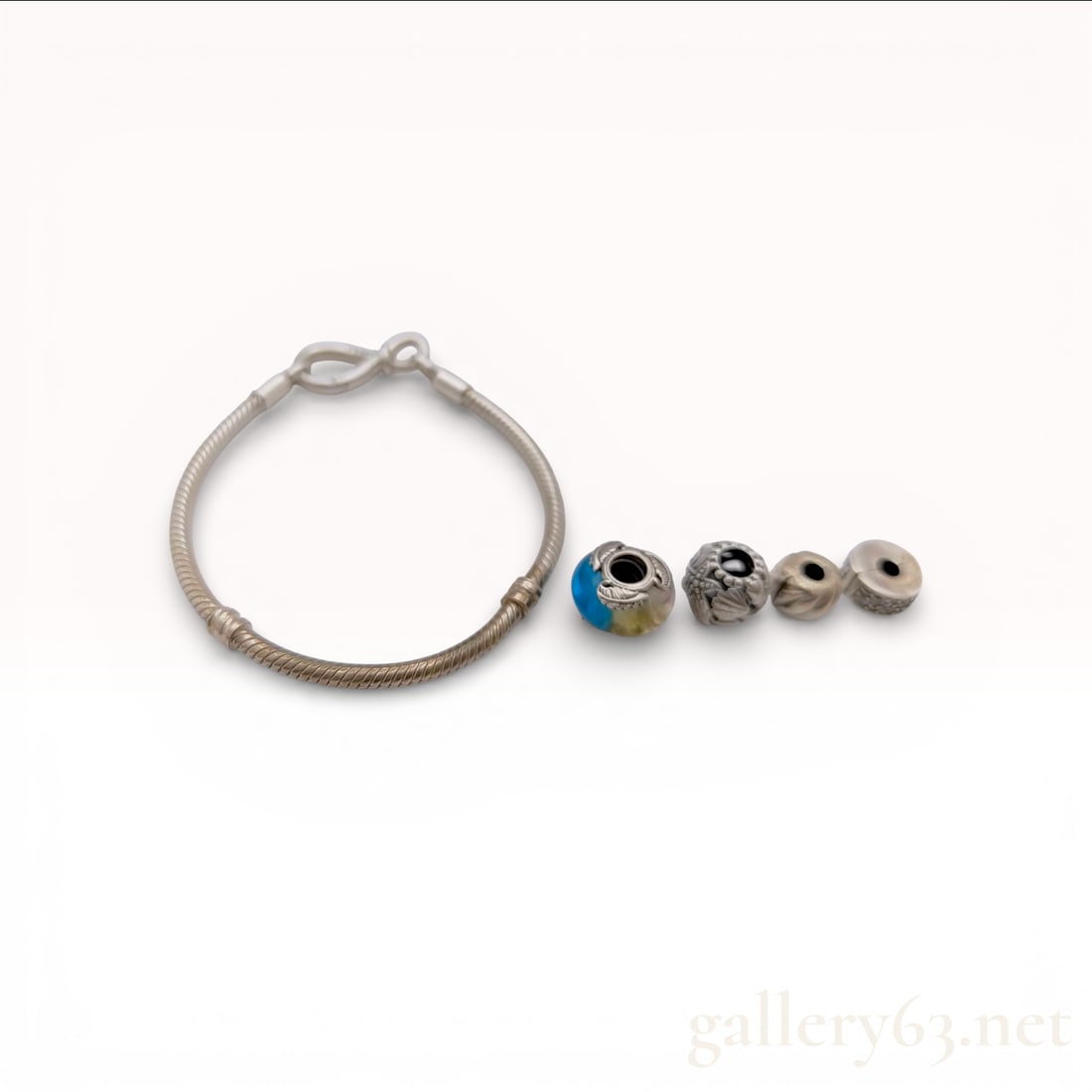 Pandora Sterling Silver Snake Chain Bracelet with Infinity Knot Clasp, Four Charms, and Box: This sterling silver snake chain bracelet by Pandora features an integrated infinity knot lobster-style clasp. The bracelet is accompanied by four charms: a Murano-style glass bead with blue and yello