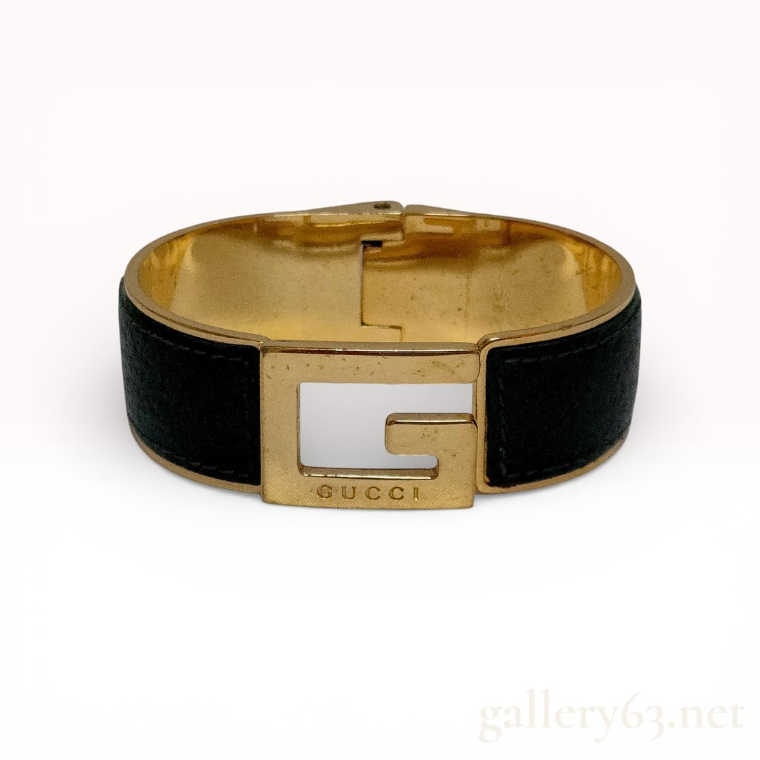 Gold-Tone and Black Leather Gucci Hinged G-Logo Bangle Bracelet: A vintage Gucci hinged bangle bracelet featuring a gold-tone metal finish and black textured leather inlays. The design is defined by a prominent, stylized G logo at the center which serves as the int