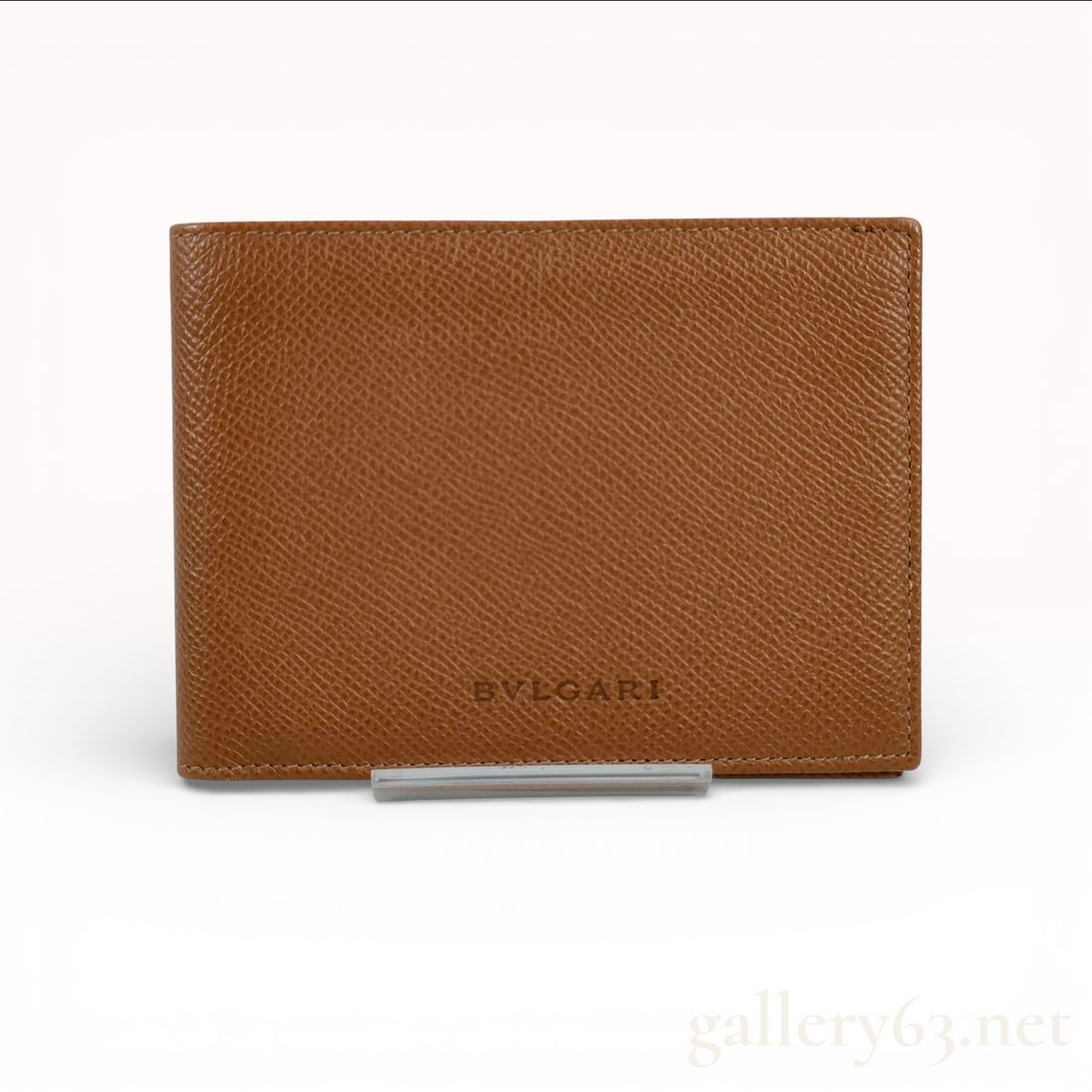 Bvlgari Bifold Wallet in Grained Cognac Leather: A professional Bvlgari bifold wallet crafted from durable grained leather in a classic cognac tan color. The front exterior features a subtle embossed logo at the lower right. The interior is