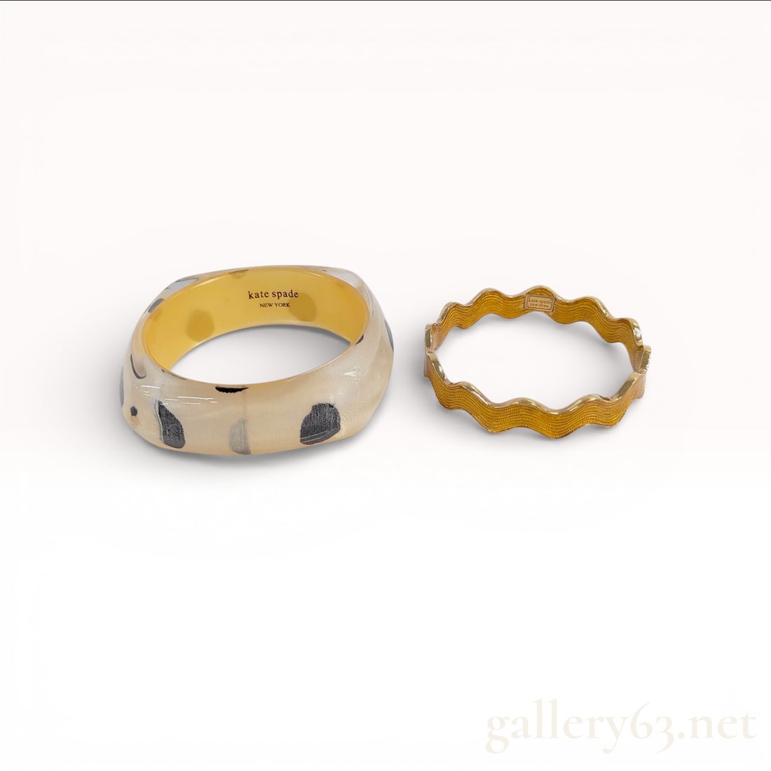 Gold-Toned and Resin Bangle Bracelet Pair, Polka Dot and Scalloped Designs: A pair of designer bangles by Kate Spade New York. The first is a wide, faceted slip-on bangle crafted from clear resin featuring an encapsulated fabric inlay with a black and gray polka dot motif on