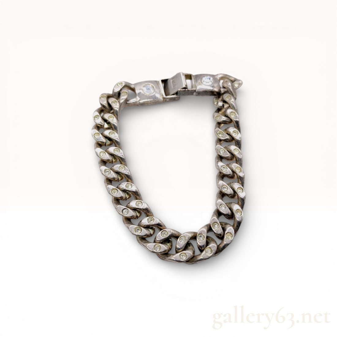 Silver-Tone Curb Link Bracelet with Rhinestone Accents: A silver-tone metal curb link bracelet, commonly referred to as a Cuban link style. The design features individual links inset with small, round colorless rhinestones. The clasp assembly is flanked by
