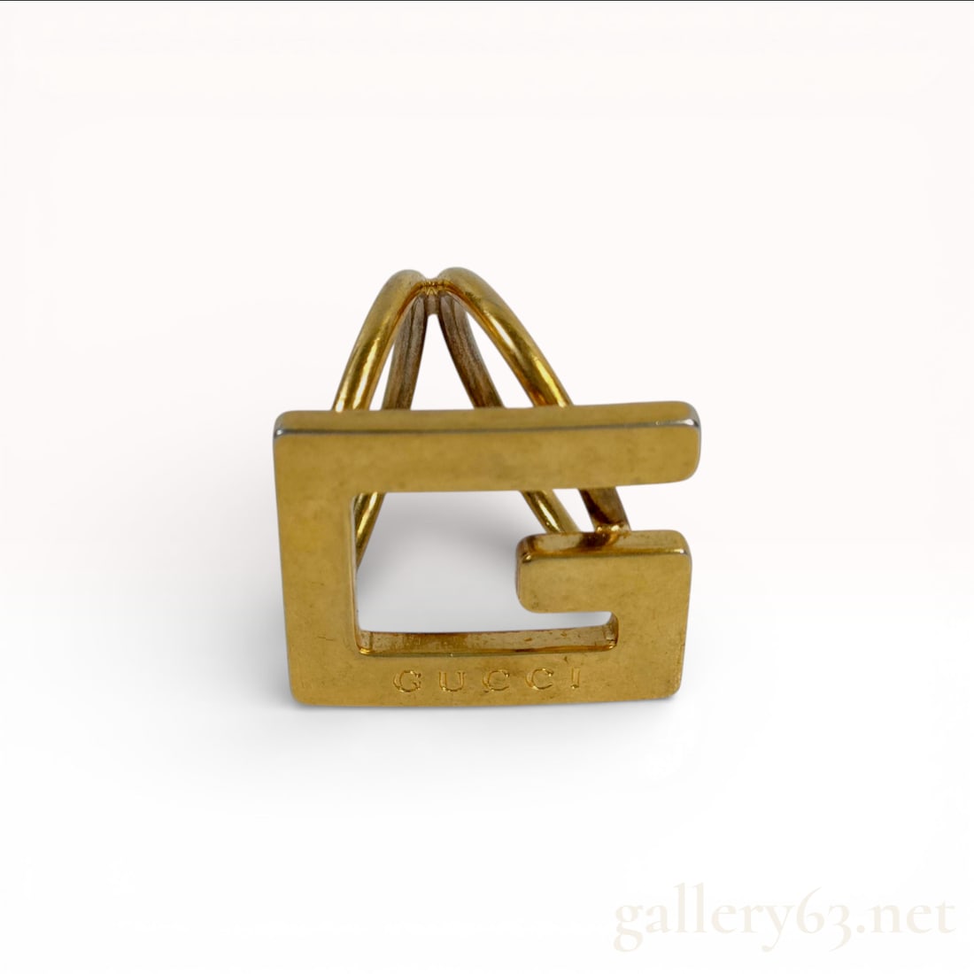 Gold-Plated Metal Gucci G Logo Scarf Ring: A Gucci G-motif scarf ring crafted in gold-plated metal. This designer accessory features the iconic square G logo on the front face, supported by a dual-band loop design intended to secure silk scarv