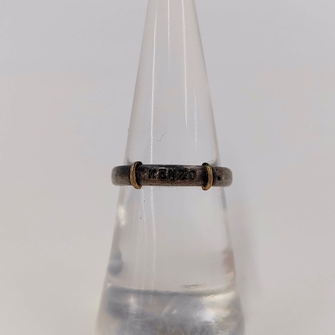 Sterling Silver & Gold Kenzo Logo Band Ring: A designer band ring by Kenzo, crafted in sterling silver. The exterior of the band features the KENZO brand name engraved in block lettering, positioned between two raised, gold-toned decorative band