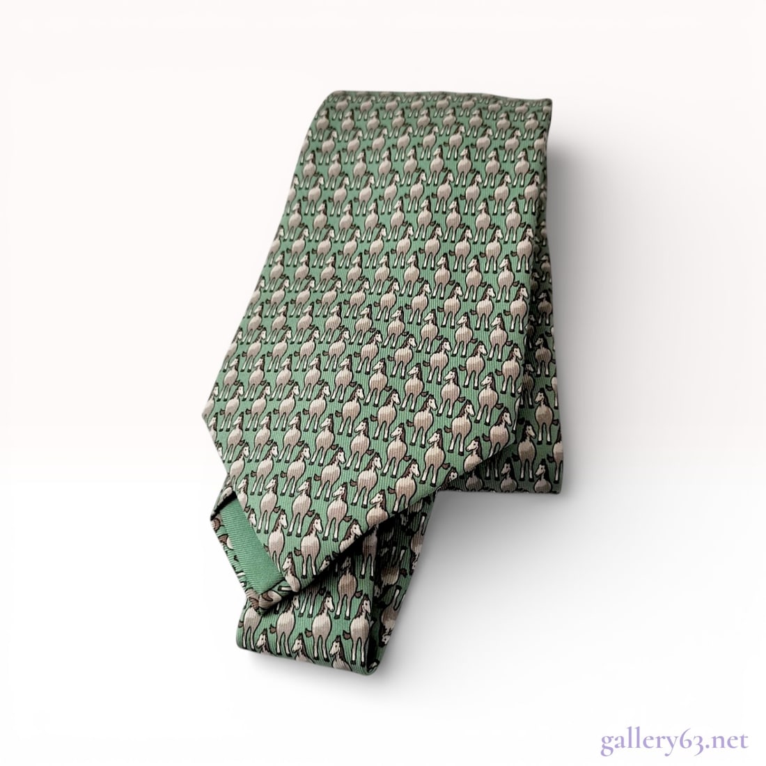 Hermes Men's Silk Necktie with Foal Pattern: A professional men's necktie by Hermes, made in France from 100% silk. The piece features a whimsical, all-over repeating pattern of foals or young horses in shades of cream and brown, set against a s