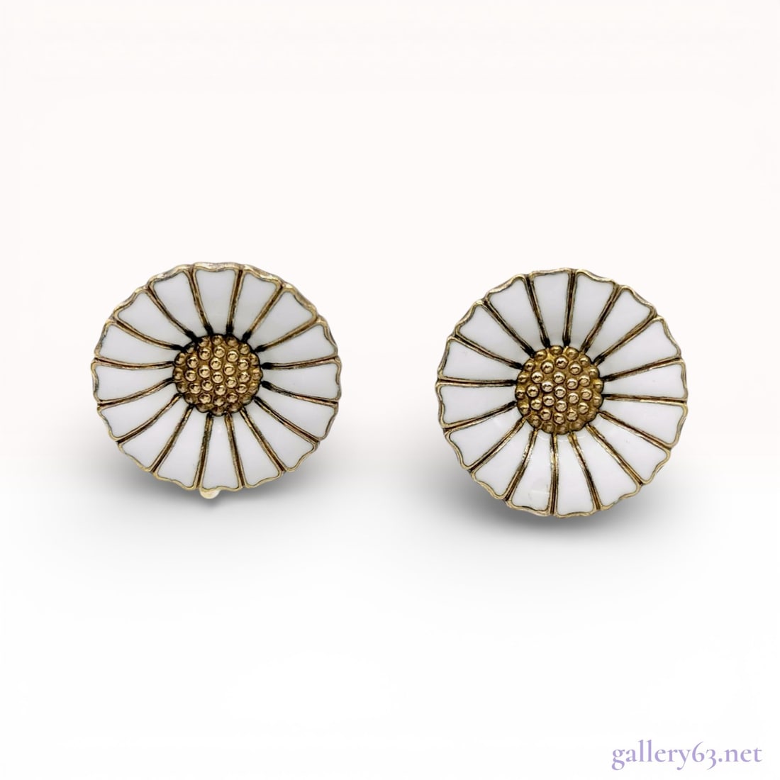 Georg Jensen Gilt Sterling Silver Screw-Back White Enamel Daisy Earrings: A matched pair of Danish modern earrings by Georg Jensen in the iconic Daisy pattern. Each earring is designed as a stylized flower featuring eighteen white vitreous enamel petals surrounding a textur
