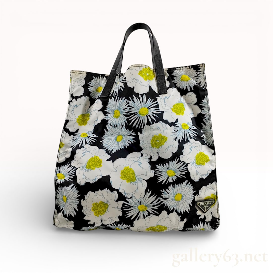 PRADA Floral Daisy Print Tessuto Nylon Tote Bag: A Prada tote bag crafted from durable black Tessuto nylon featuring an all-over stylized daisy floral print in white and yellow. The exterior is accented with the signature enameled triangle logo on t