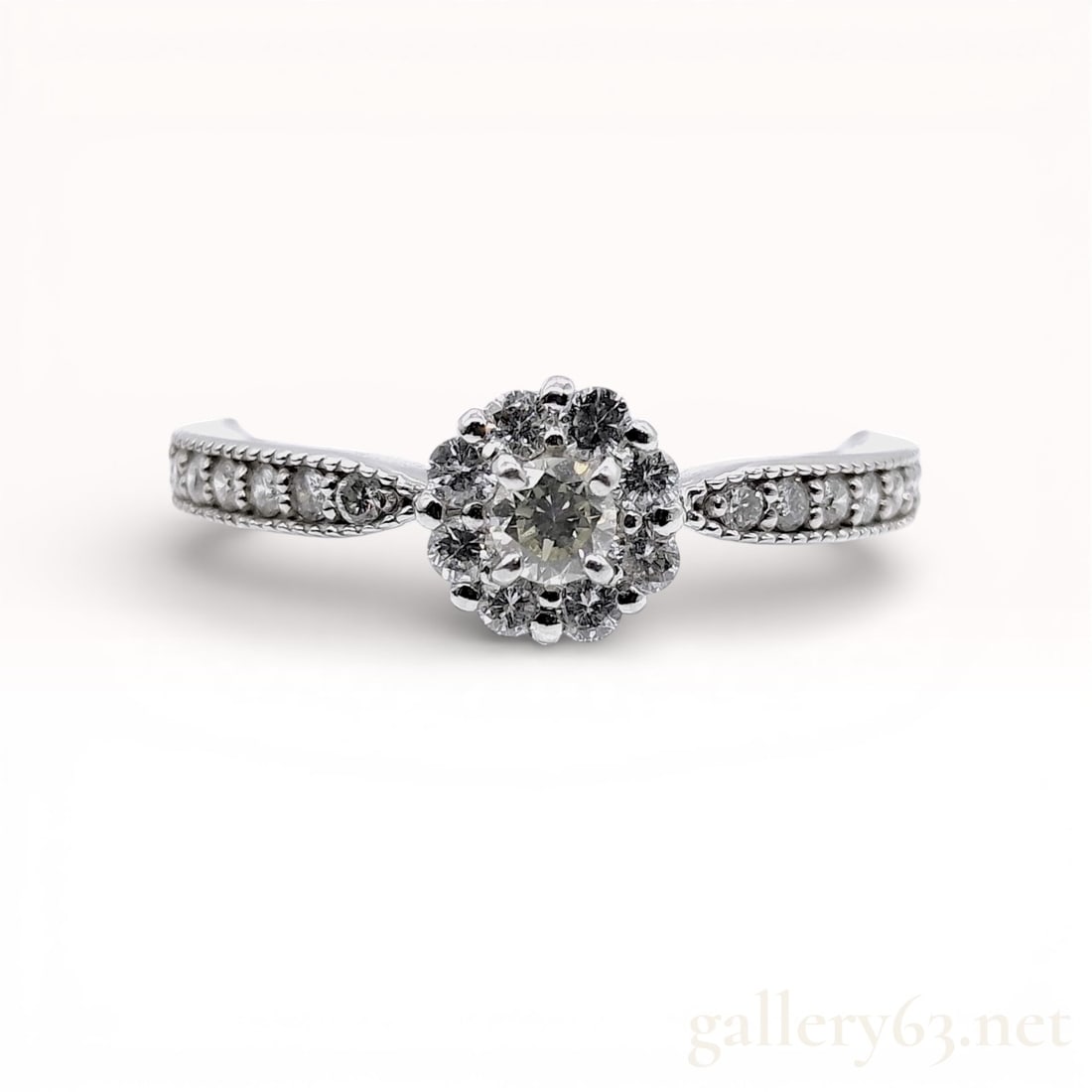 Platinum Diamond Halo Cluster Ring: A platinum diamond halo cluster ring featuring a round brilliant cut center diamond weighing approximately 0.10 carats. The center stone is secured by four double-prongs and surrounded by a halo of