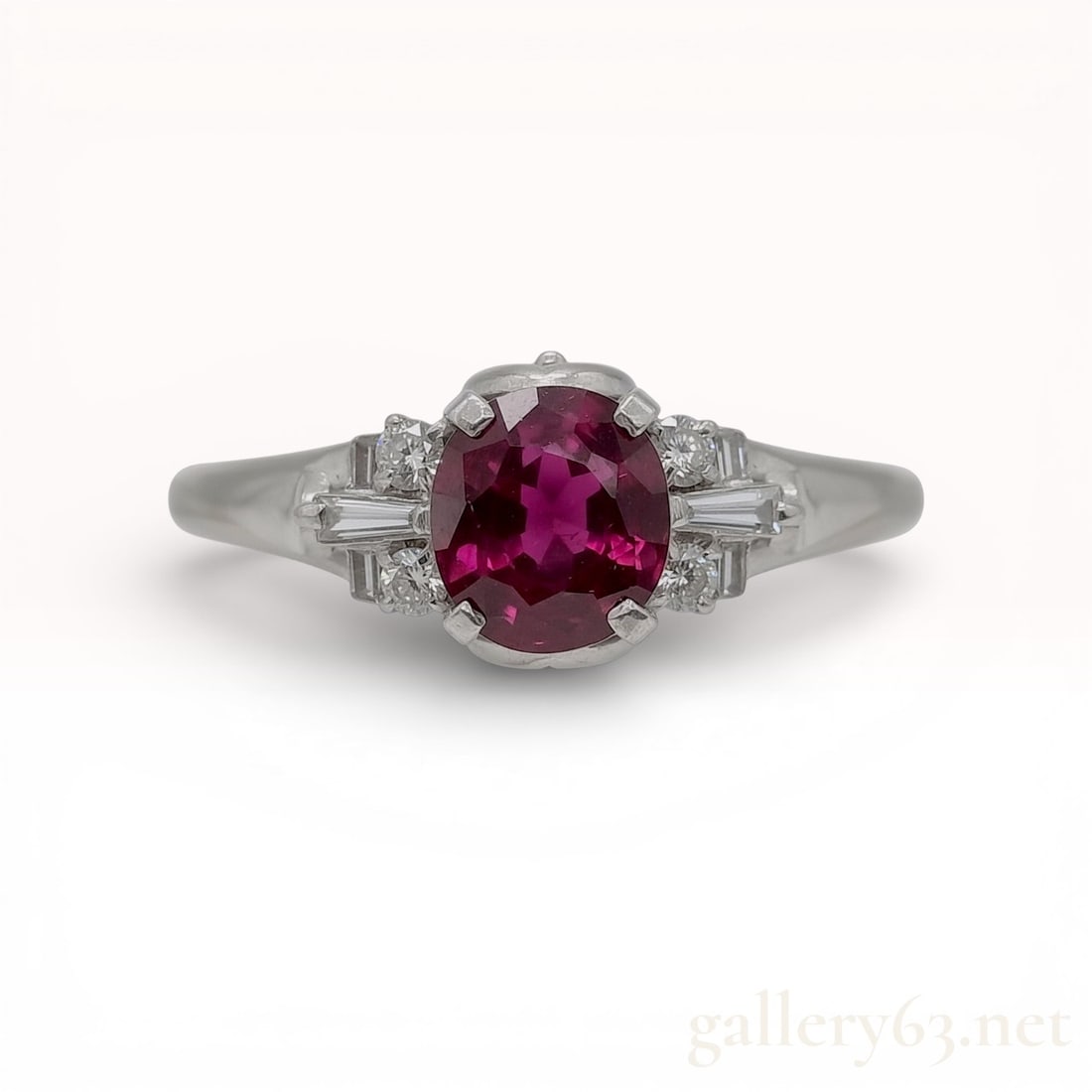 Platinum, Ruby, and Diamond Cocktail Ring: An estate platinum cocktail ring featuring a central oval-cut ruby. The ruby displays a vibrant pinkish-red color with visible natural inclusions and is secured in a four-prong basket setting. The cen