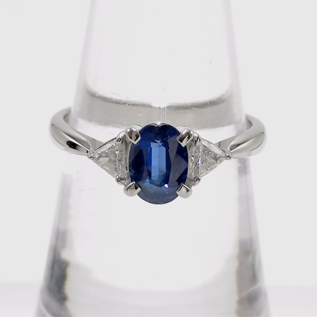 Pt900 Platinum Sapphire and Diamond Three-Stone Ring: This elegant three-stone ring is crafted in Pt900 platinum and features a central oval-cut blue sapphire. The center stone is secured by a four-double-prong setting and is complemented by two