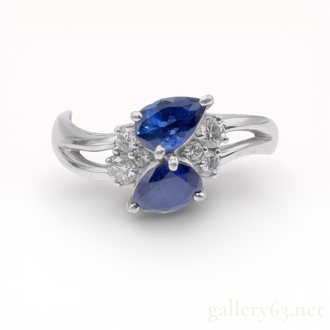 Platinum Sapphire and Diamond Crossover Ring: This cocktail ring is crafted in Pt900 platinum and features a modern bypass or "Moi et Toi" crossover design. The center is set with two pear-cut blue sapphires. According to the interior