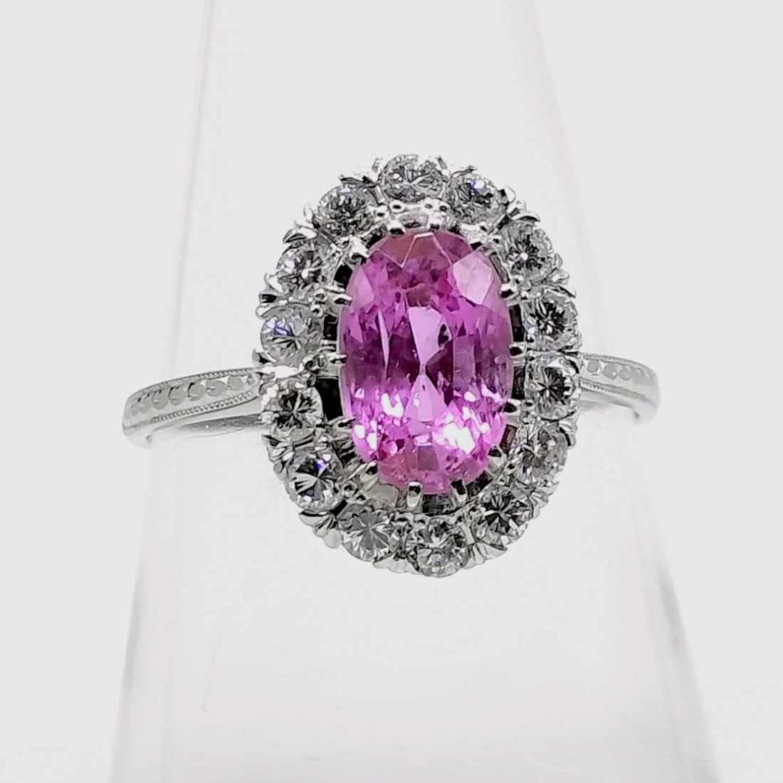 Platinum Oval Pink Sapphire and Diamond Halo Cocktail Ring, size 6.25: A vintage cocktail ring crafted in platinum, featuring a central oval-cut vibrant pink sapphire. The gemstone is secured by four split prongs and surrounded by a halo of fourteen round brilliant-cut d