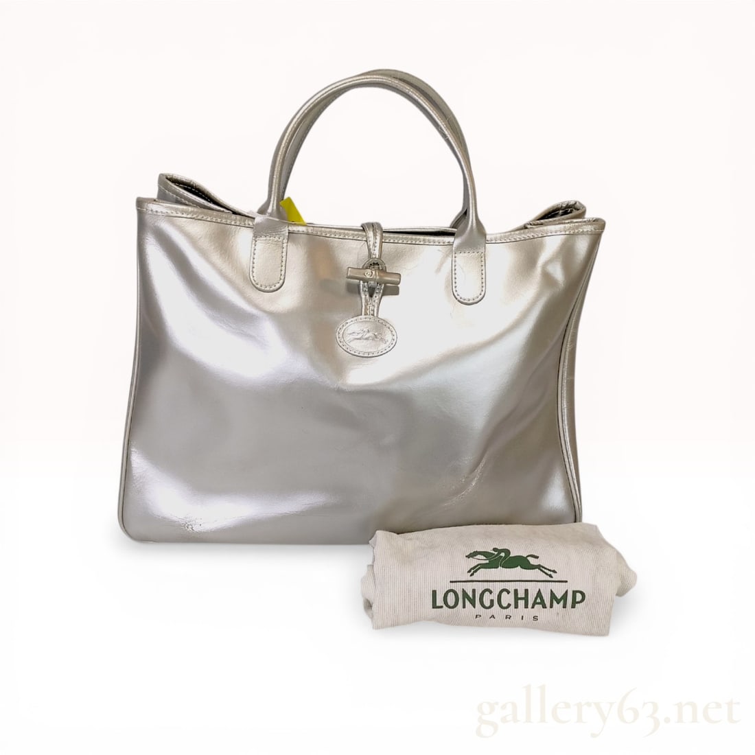 Longchamp Roseau Metallic Leather Tote Bag: Longchamp Roseau tote bag in silver metallic leather. The bag features the signature silver-tone bamboo-style toggle closure and an embossed oval horse logo emblem on the front. Construction includes