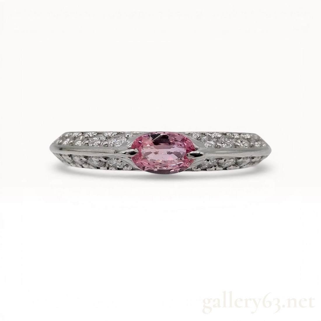 Platinum Pink Sapphire and Diamond Dress Ring: Modern platinum dress ring featuring a central pink gemstone and diamond accents. The horizontally oriented oval-cut pink sapphire is held in a semi-bezel setting, flanked by tapered shoulders pav&eac