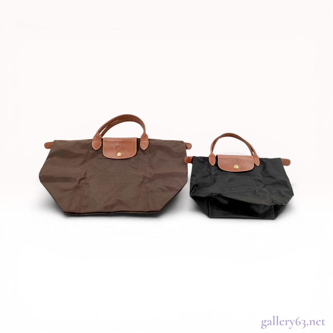 Two Longchamp Le Pliage Nylon and Leather Foldable Tote Bags: Longchamp Le Pliage foldable tote bags. The lot features one large brown nylon bag and one small black nylon bag, both with textured brown Russian leather handles and top flaps. Each bag includes gold