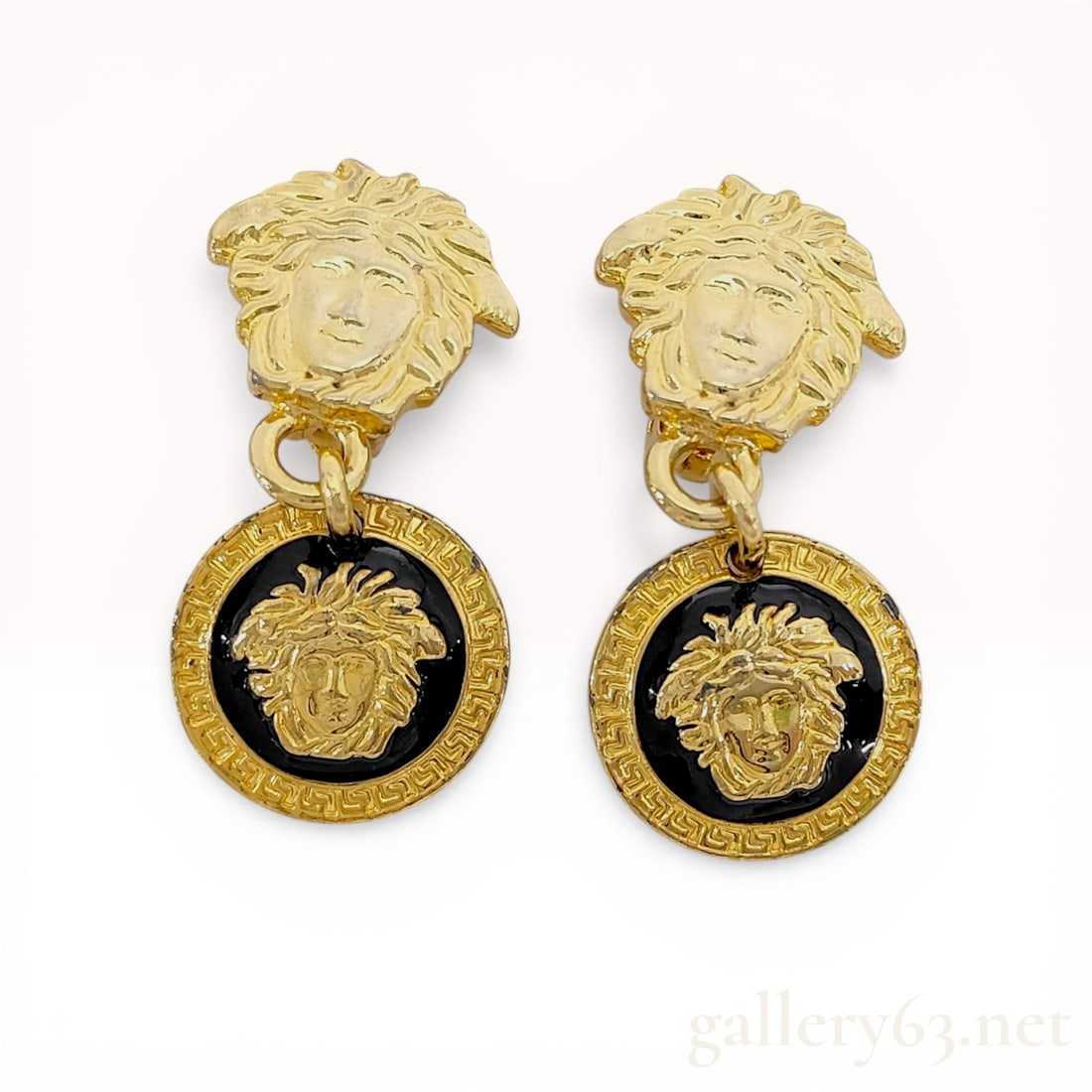 A Pair of Vintage Gianni Versace Medusa Enamel Drop Earrings: Gianni Versace gold-toned drop earrings featuring a Medusa head top and reversible circular medallion drops. The medallions display a Medusa head against black enamel on one side and white enamel on t